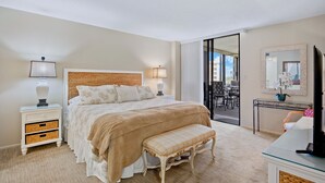 A hotel room with a large bed, bedside lamps, a bench, a TV, and a view of the outside balcony.