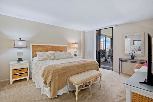 A hotel room with a large bed, bedside lamps, a bench, a TV, and a view of the outside balcony. - Gulf and Bay Club - 410 - 3 Pools! (Siesta Key)
