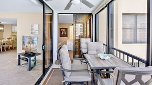 A modern hotel room with a balcony, a ceiling fan, a dining area with a table and chairs, and a television on a stand. - Gulf and Bay Club - 410 - 3 Pools! (Siesta Key)