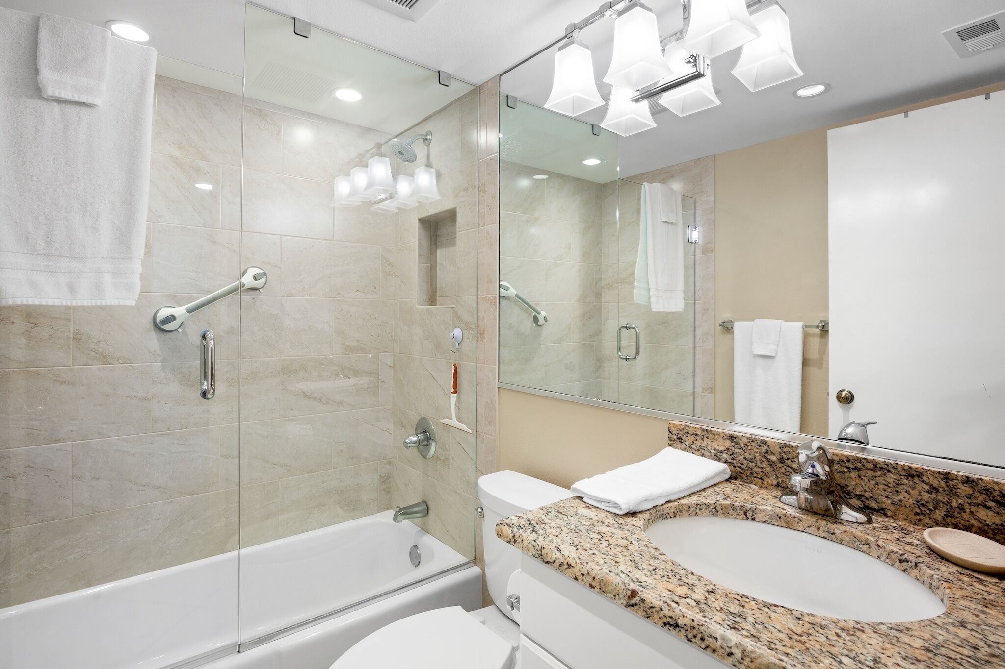 Une salle de bain moderne avec une douche à parois de verre, un lavabo sur un plan de travail en granit et un grand miroir.