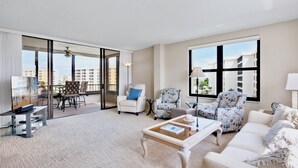 A spacious living room with a large window, a balcony, and a seating area with a coffee table and sofas.