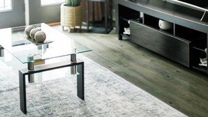 Una sala de estar moderna con una mesa de centro de vidrio, un televisor de pantalla plana, una planta en maceta y una estantería.