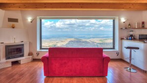Une pièce dotée d’une grande fenêtre donnant sur un paysage, d’un canapé rouge, d’une cheminée et d’un coin cuisine avec un tabouret de bar.