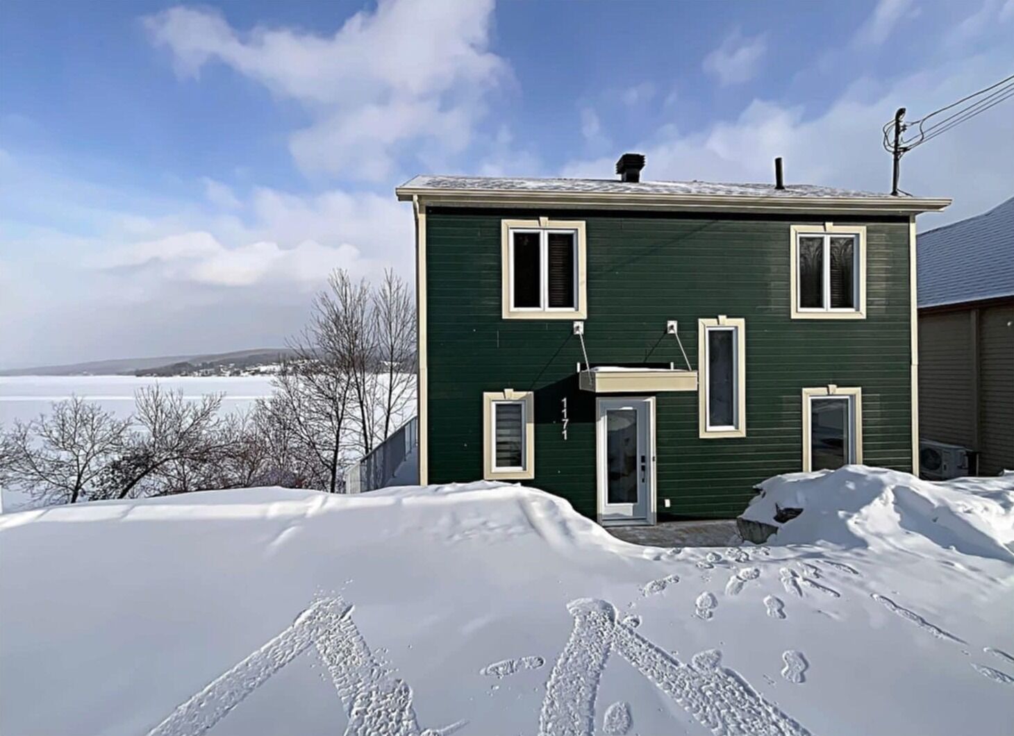 Une maison verte avec un garage, une véranda et une vue sur un lac gelé.