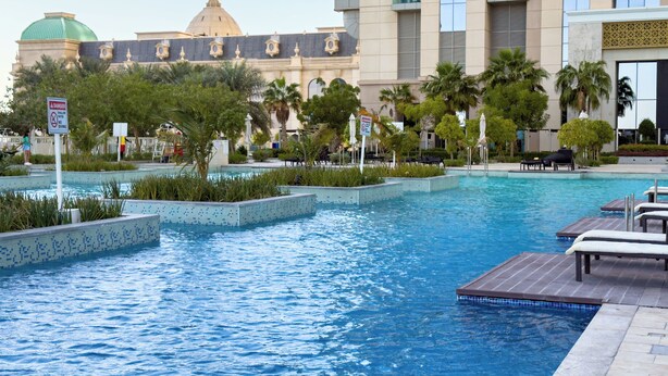 A swimming pool with lounge chairs and palm trees, surrounded by a building with a dome and a modern structure. - Modern 2BR | 60th Floor Views in Business Bay (دبي)