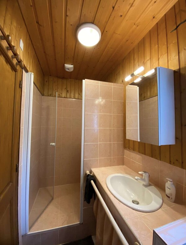 A wooden-paneled bathroom with a shower, a sink, and a mirror.