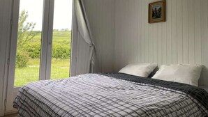 A bedroom with a bed, a window with curtains, and a painting on the wall.
