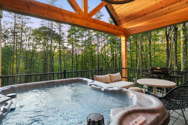 Un espace avec un bain à remous et une terrasse en bois, entouré d’une forêt.
