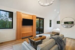 Un salon moderne doté d’un grand téléviseur à écran plat, de meubles en bois, d’un canapé et d’un grand miroir rond accroché au mur.
