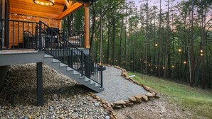 A wooden cabin with a covered porch, stone steps, and a gravel path leading to a forest. - Nature's Loft | Hocking Hills, New Modern Cabin (Rockbridge)