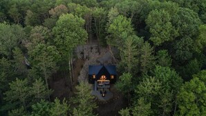 An aerial view of a cabin surrounded by dense forest, with a clear sky and distant hills. - Nature's Loft | Hocking Hills, New Modern Cabin (Rockbridge)