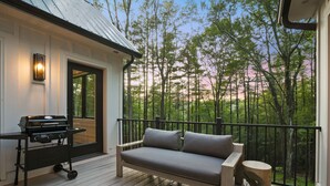 A wooden deck with a grill, a sofa, and a view of a forest. - The U Haus | Hocking Hills, Modern & New, Hot Tub (Rockbridge)