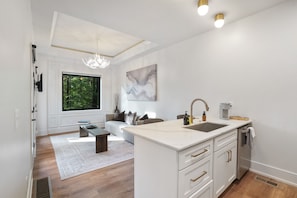 A modern kitchen with a large window, a dining area with a sofa, and a white island with a sink.