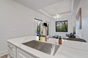 Una cocina moderna con un lavamanos grande de acero inoxidable, armarios blancos y una lámpara de araña.