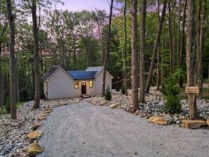 Una cabaña con camino de entrada de grava, rodeada de árboles y un letrero que dice "The U Haus".