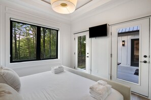 Un dormitorio con una ventana grande, un televisor de pantalla plana y una puerta al balcón.