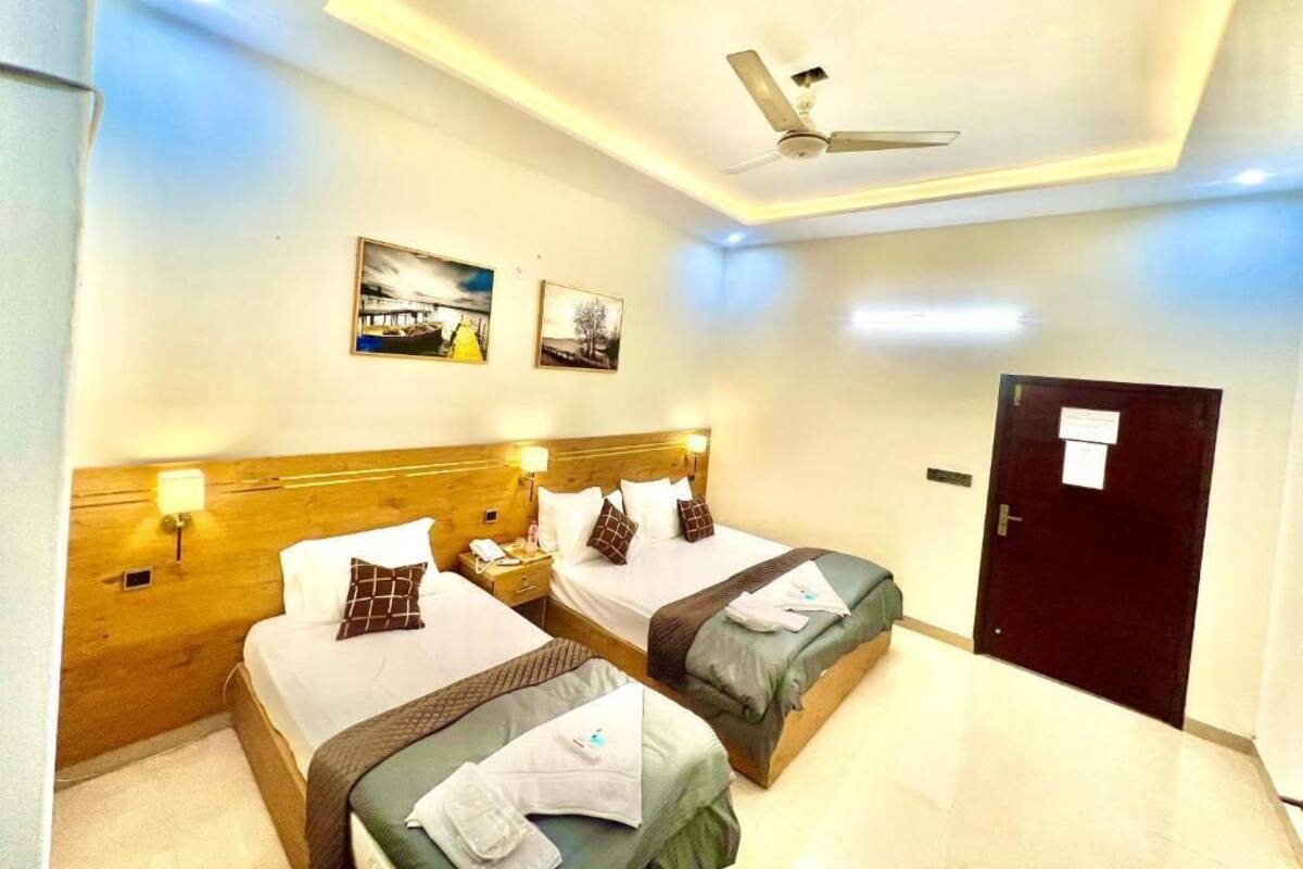 A hotel room with two beds, a ceiling fan, and artwork on the walls.