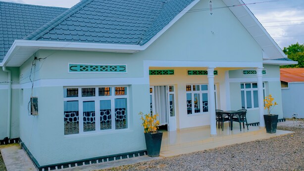 A two-story house with a tiled roof, white exterior walls, and a covered patio area with a table and chairs. - Peaceful apartment with WiFi in charming Musanze-down town. (Musanze)