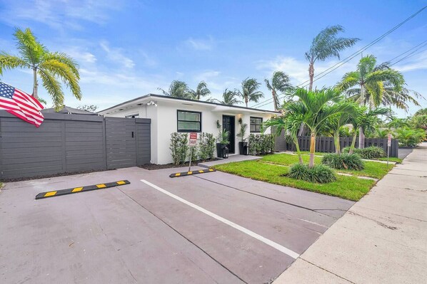 A residential property with a gated driveway, a well-maintained lawn, and a small house with a front door and windows.
