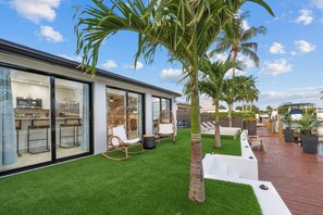 A modern house with a glass exterior, a patio with outdoor seating, and a well-maintained lawn.