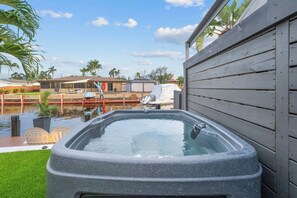 A hot tub with a view of a pool and a wooden deck. - Waterfront Duplex Tropical Oasis (Dania Beach)
