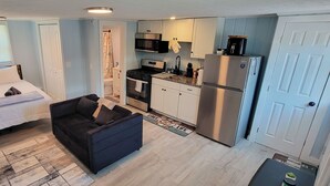 Una habitación compacta con cama, sofá, kitchenette y baño.