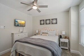 Une chambre à coucher avec un lit, un téléviseur, un ventilateur de plafond et des œuvres d’art accrochées au mur.