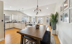 A spacious kitchen with a central island, a dining area with a wooden table, and a living room with a sofa and a large plant.