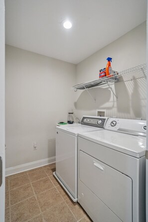 Une buanderie équipée d’un lave-linge, d’un sèche-linge et d’une étagère sur laquelle se trouve une bouteille.