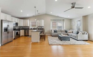 A spacious kitchen with modern appliances, a dining area with a large island, and a living room with a sectional sofa and a ceiling fan.