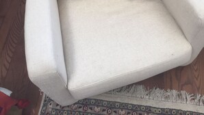 Un sillón blanco con un peluche con camisa roja.
