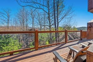 A wooden deck with a metal railing overlooking a forested area.