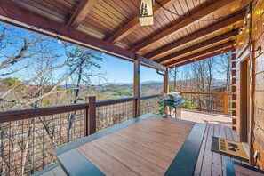 A wooden deck with a grill, a view of the landscape, and a wooden railing.