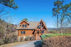 A two-story wooden cabin with a prominent gable roof, a front porch, and a stone foundation.