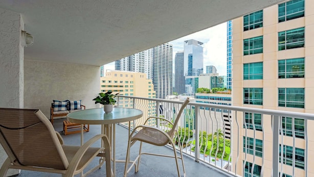A balcony with a round table and two chairs, a potted plant, and a view of tall buildings.