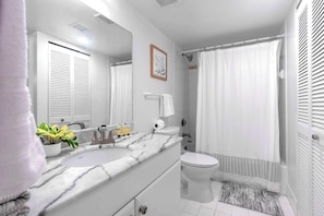 A modern bathroom with a white vanity, a sink, a toilet, and a shower area.