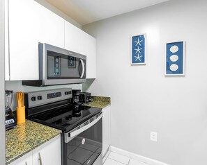 A modern kitchen with white cabinets, a black stove, a microwave, and a coffee maker. There are two blue wall art pieces with star and circle designs. - Grand 1BR | Free Parking | Near Bayfront Park (Miami)