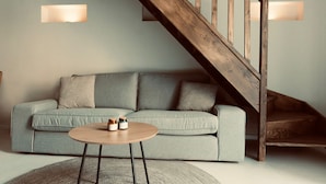 Un soggiorno moderno con un divano grigio, un tavolino rotondo in legno e una scala in legno.