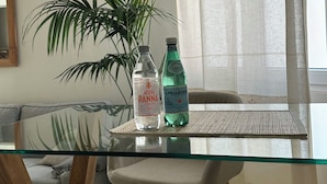 Un tavolo in vetro con due bottiglie d'acqua, un lampadario intrecciato e una pianta in vaso.