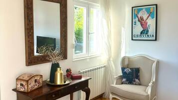 Une chambre à coucher avec un lit, une chaise, un bureau, un miroir et une fenêtre avec des rideaux.