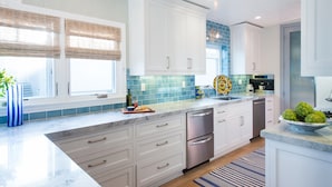 A modern kitchen with white cabinets, a marble countertop, and a blue backsplash.