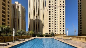 Una piscina rectangular con solárium empedrado, rodeada de edificios altos.