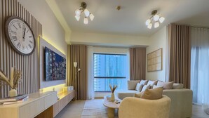 Una sala de estar moderna con un reloj grande, un conjunto de sofás, una mesa de centro y vistas de la ciudad a través de amplias ventanas.