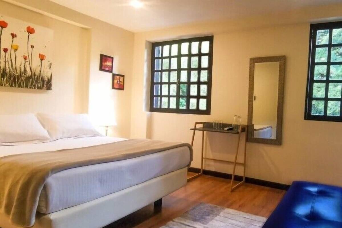 Un dormitorio con cama, escritorio y ventana con vistas a árboles.