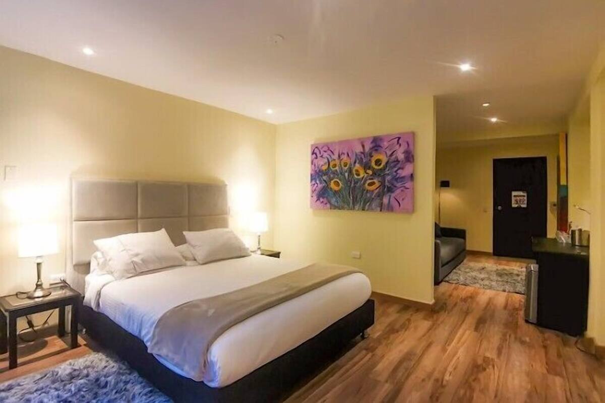 Una habitación de hotel con una cama, mesitas de noche, un cuadro, un escritorio y una silla.