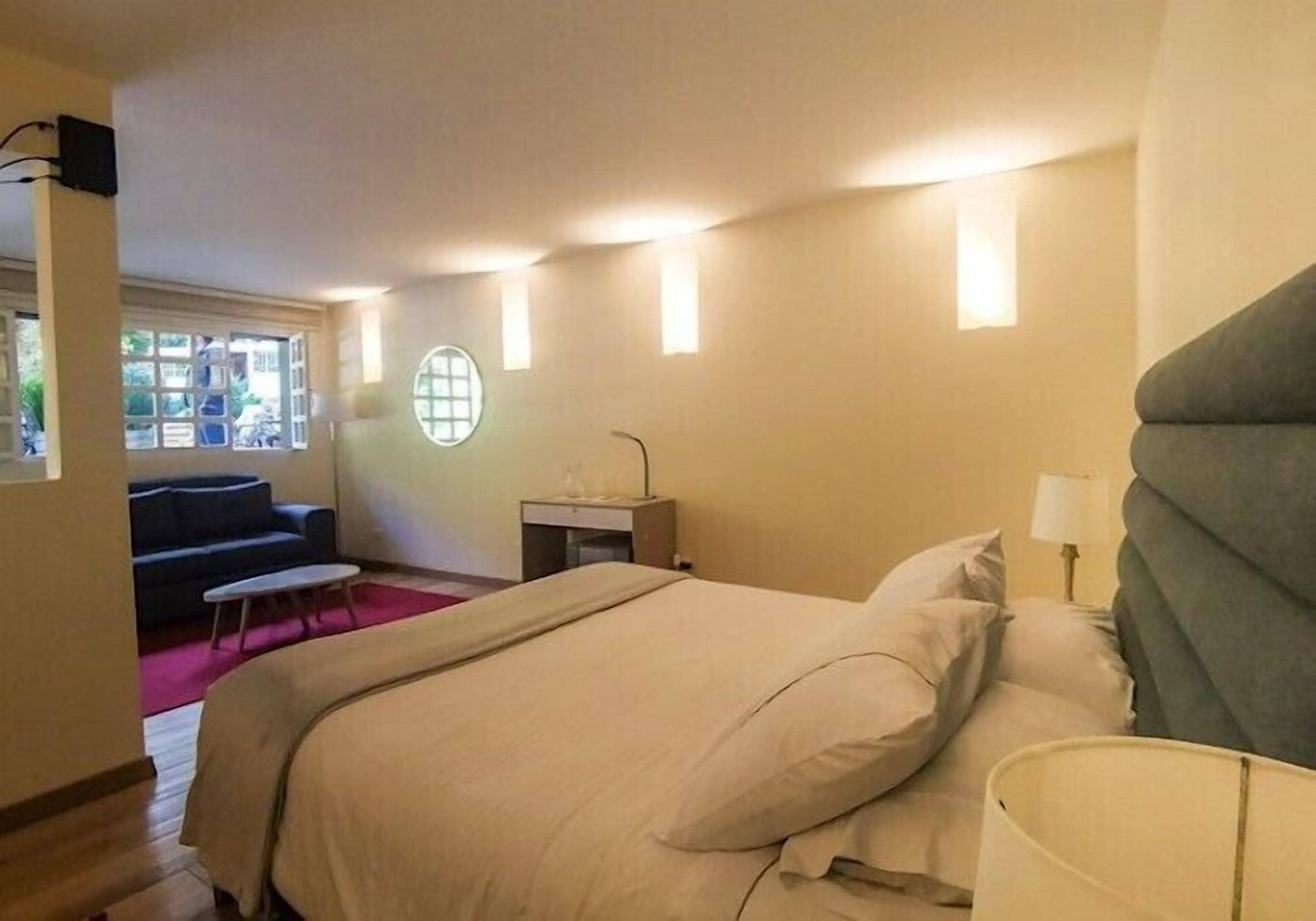 Un dormitorio con cama, mesita de noche, lámpara y vistas al exterior.