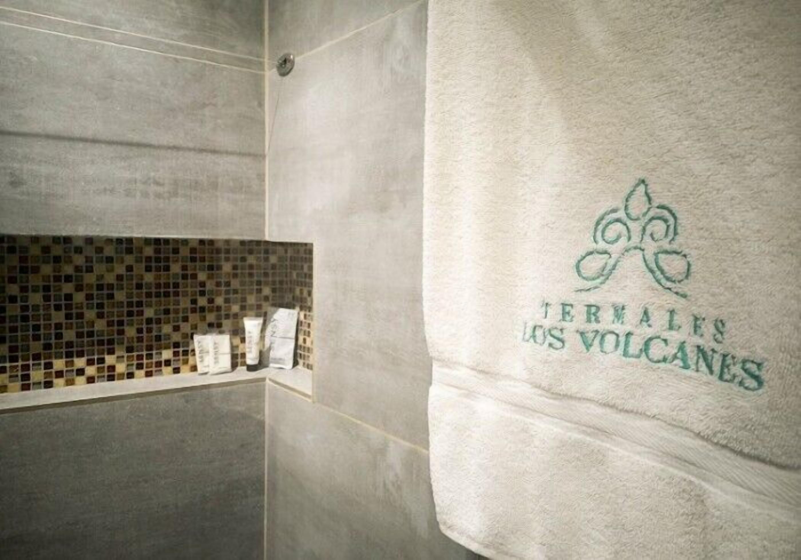 Un baño con zona de ducha azulejada y una toalla con logotipo y texto.