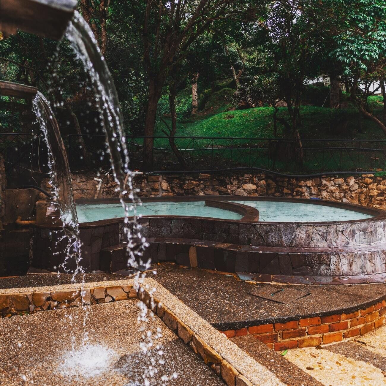 A water feature with a cascading stream, a circular hot tub, and a stone wall surrounding the area.