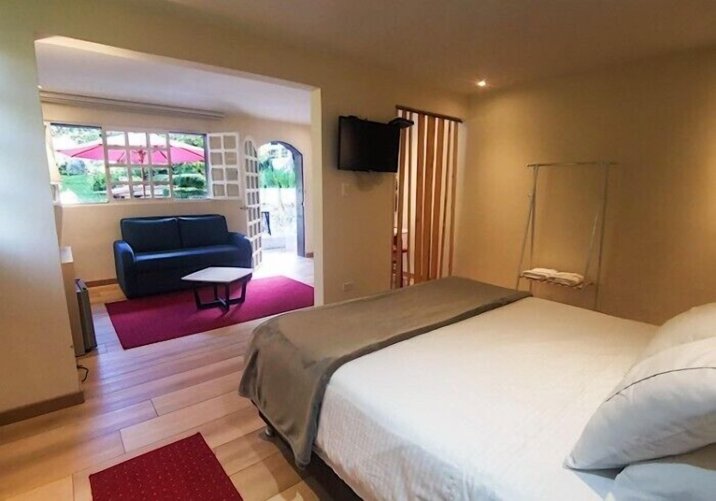 Un dormitorio con cama, televisor montado en la pared, ventana con cortinas y vistas al exterior.
