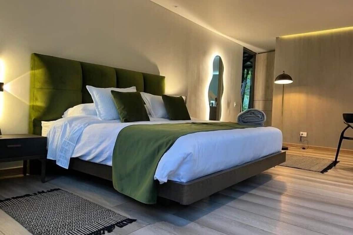 Un dormitorio moderno con una cama grande, cabecera tapizada de verde y una mesita de noche.